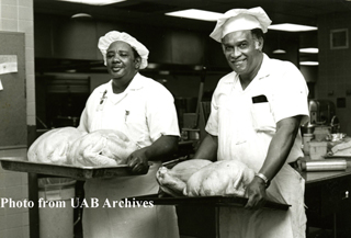 Two male kitchen workers carry turkeys ready to be cooked