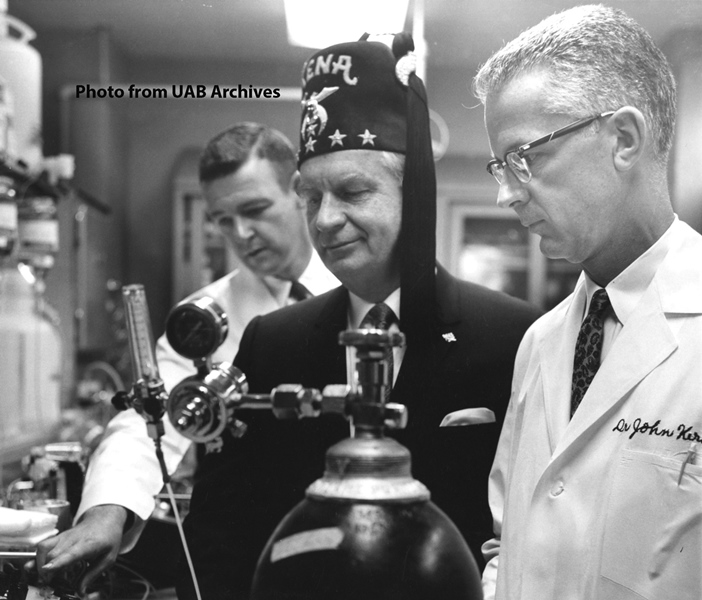 A shriner stands between two physicians examining equipment