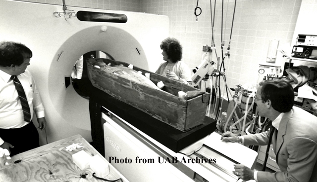 A mummy enters a cat scan machine as three people watch
